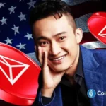 Foto de Justin Sun sorrindo em terno azul com logos vermelhos da TRON ao fundo da bandeira americana, representando a estreia da empresa na Nasdaq.