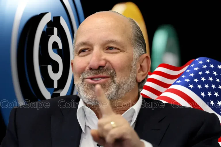 Howard Lutnick sorrindo e apontando para a câmera, com símbolo do dólar e bandeira americana ao fundo
