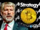 Montagem com Michael Saylor ao lado de moeda de Bitcoin dourada sobre fundo da marca Strategy