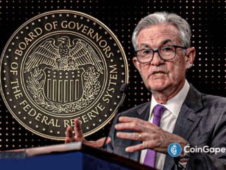Jerome Powell falando em coletiva de imprensa com o selo do Federal Reserve ao fundo, gesticulando durante explicações sobre decisões de política monetária.