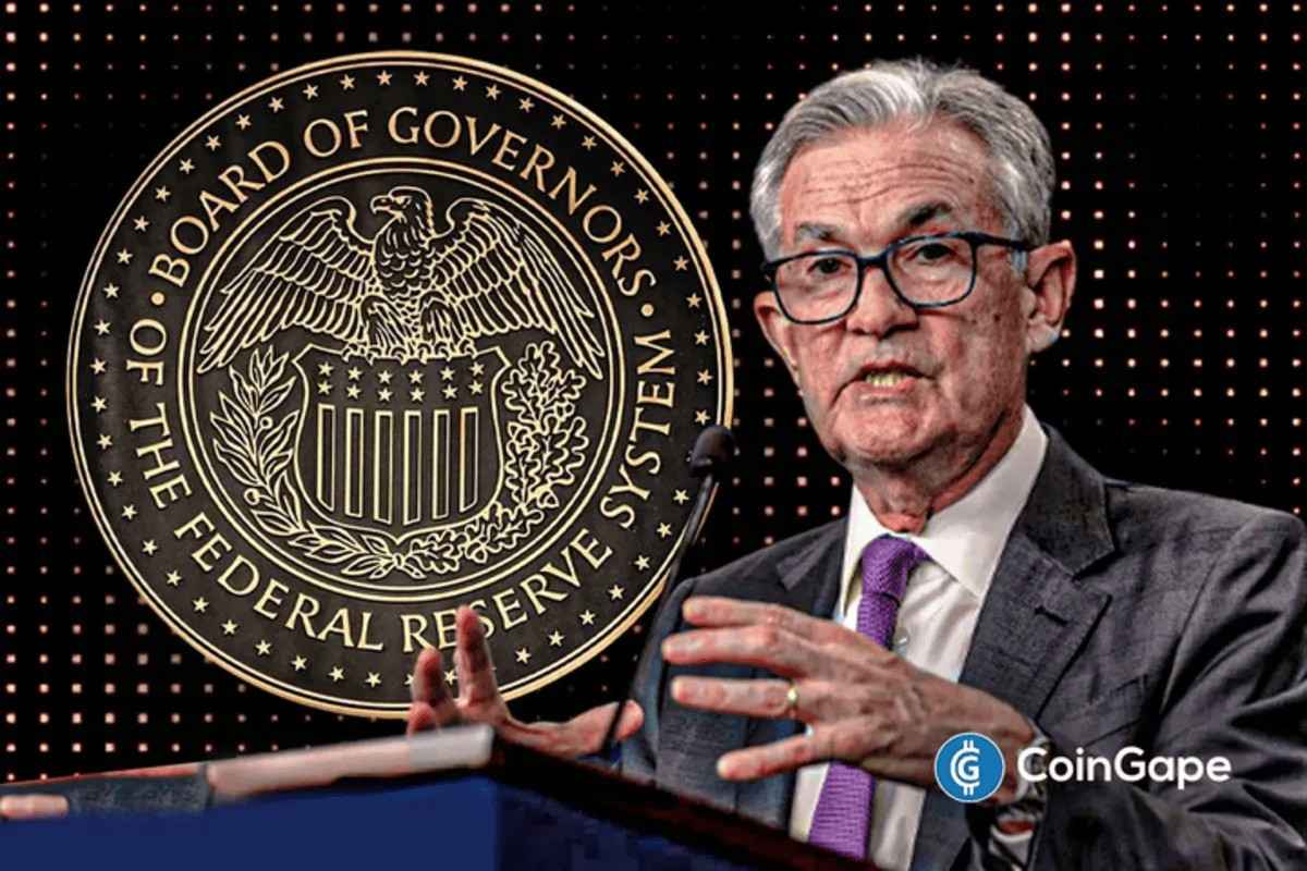 Jerome Powell falando em coletiva de imprensa com o selo do Federal Reserve ao fundo, gesticulando durante explicações sobre decisões de política monetária.