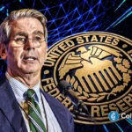 Jerome Powell em frente ao selo do Federal Reserve System com fundo digital azul e logo do CoinGape.